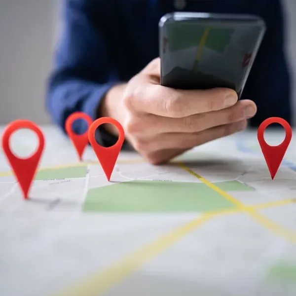 Hand holding a smartphone above a map with red location pins, suggesting route planning or navigation