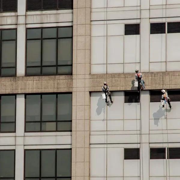 Three climbers in helmets rappelling down a high-rise building facade