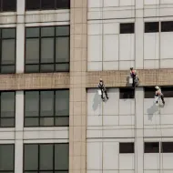 Three climbers in helmets rappelling down a high-rise building facade