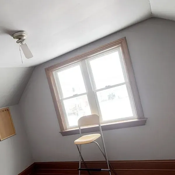 Small empty room with a folding chair by a bright window and a slanted ceiling