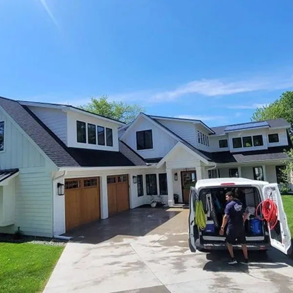 Suburban house with open van rear door, two people unloading items from the driveway.