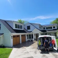 Suburban house with open van rear door, two people unloading items from the driveway.