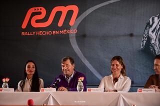 Un grupo de personas está sentado en una mesa frente a un cartel que dice rally hecho en mexico.