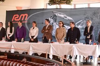 Un grupo de personas está de pie en una mesa frente a un cartel que dice rem.