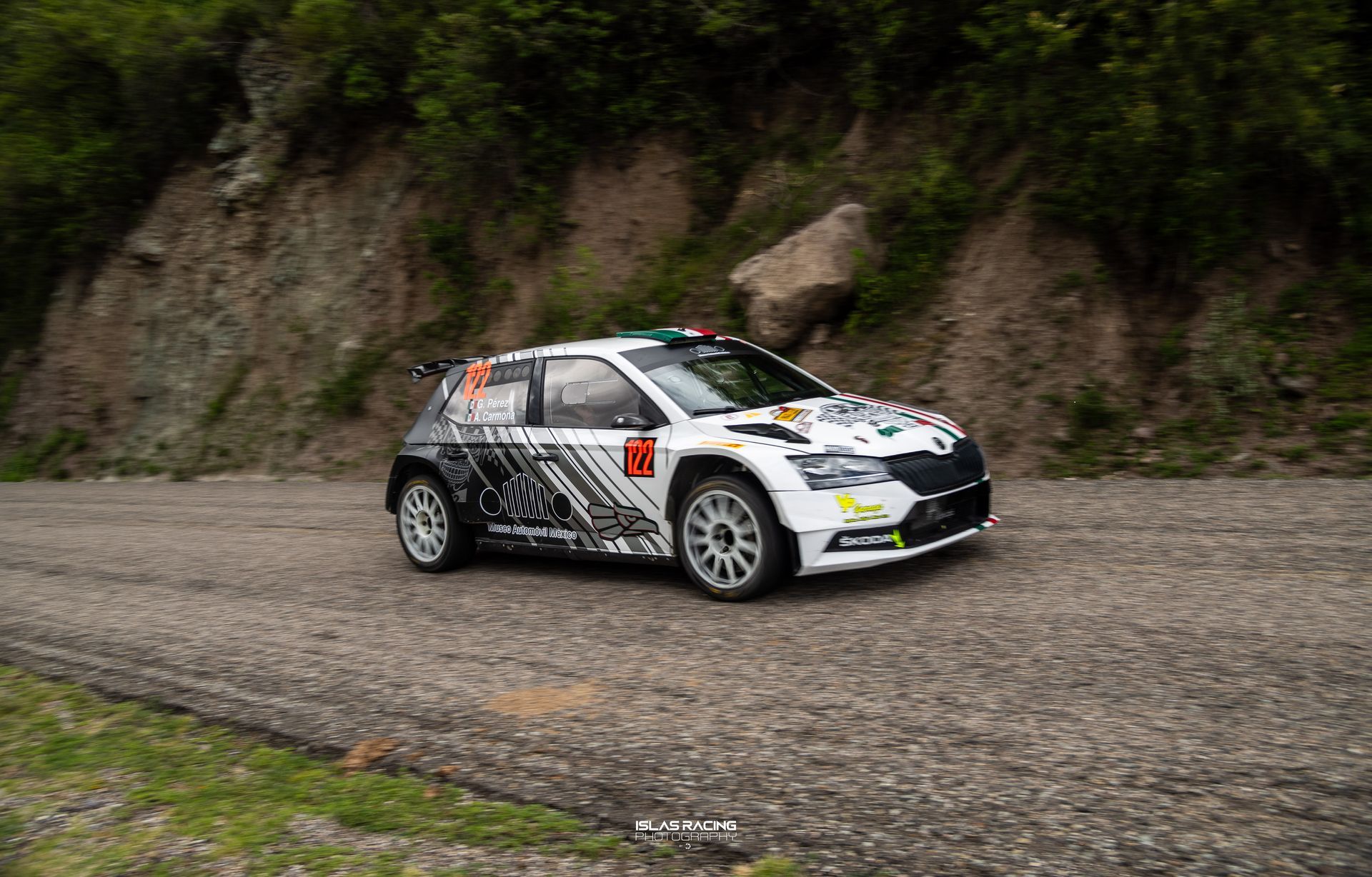 Un coche de rally blanco circula por un camino de tierra.