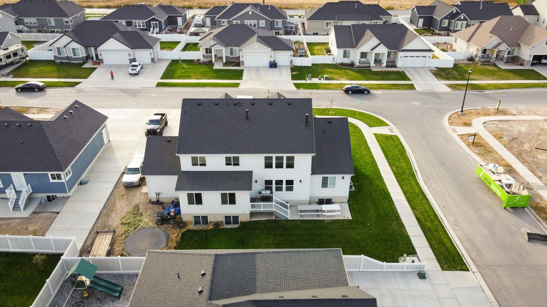 Aerial view of a suburban neighborhood with a large white house, driveway, and rows of homes along a curved street