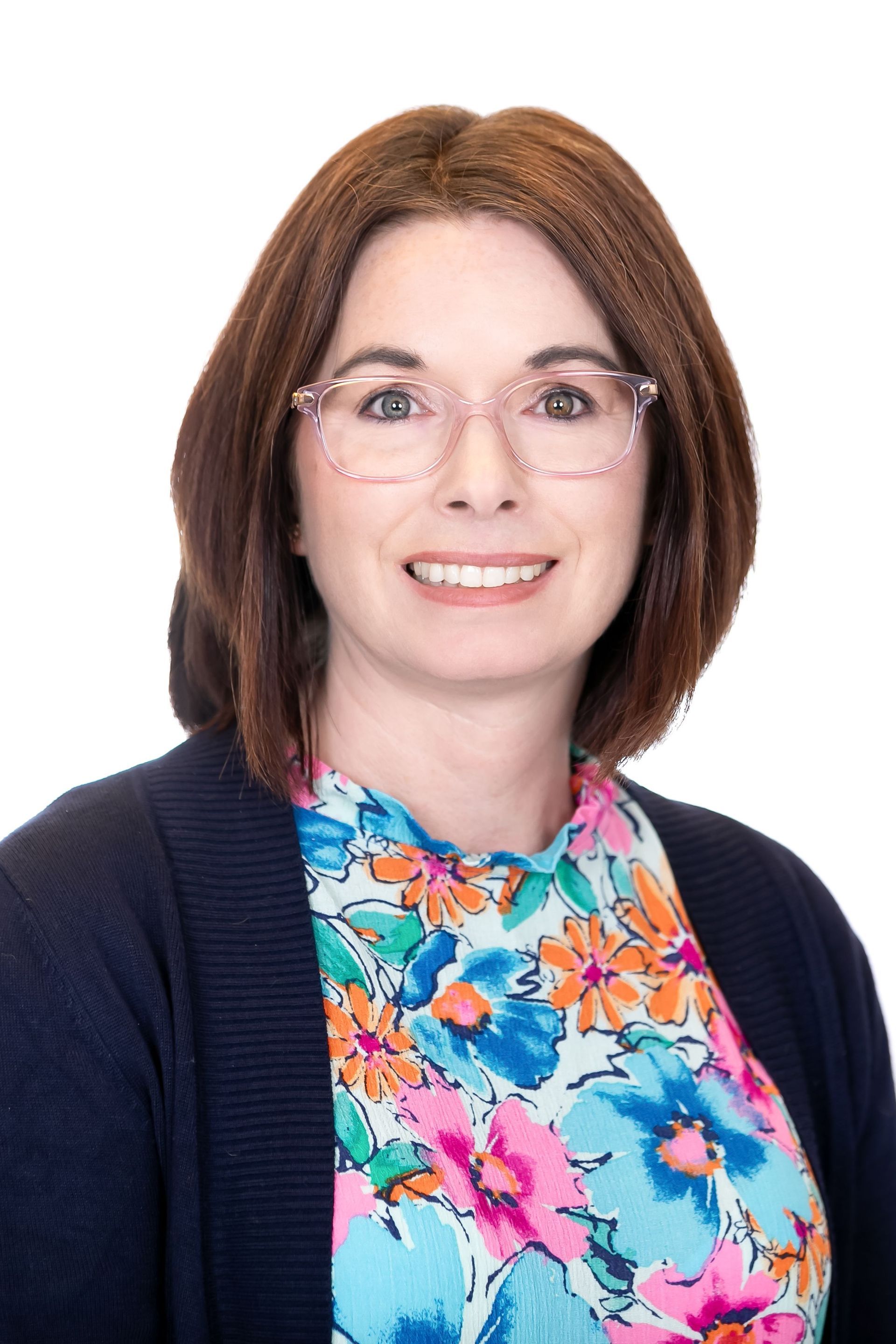 Portrait of a smiling person with glasses, dark cardigan, and colorful floral blouse on a white background