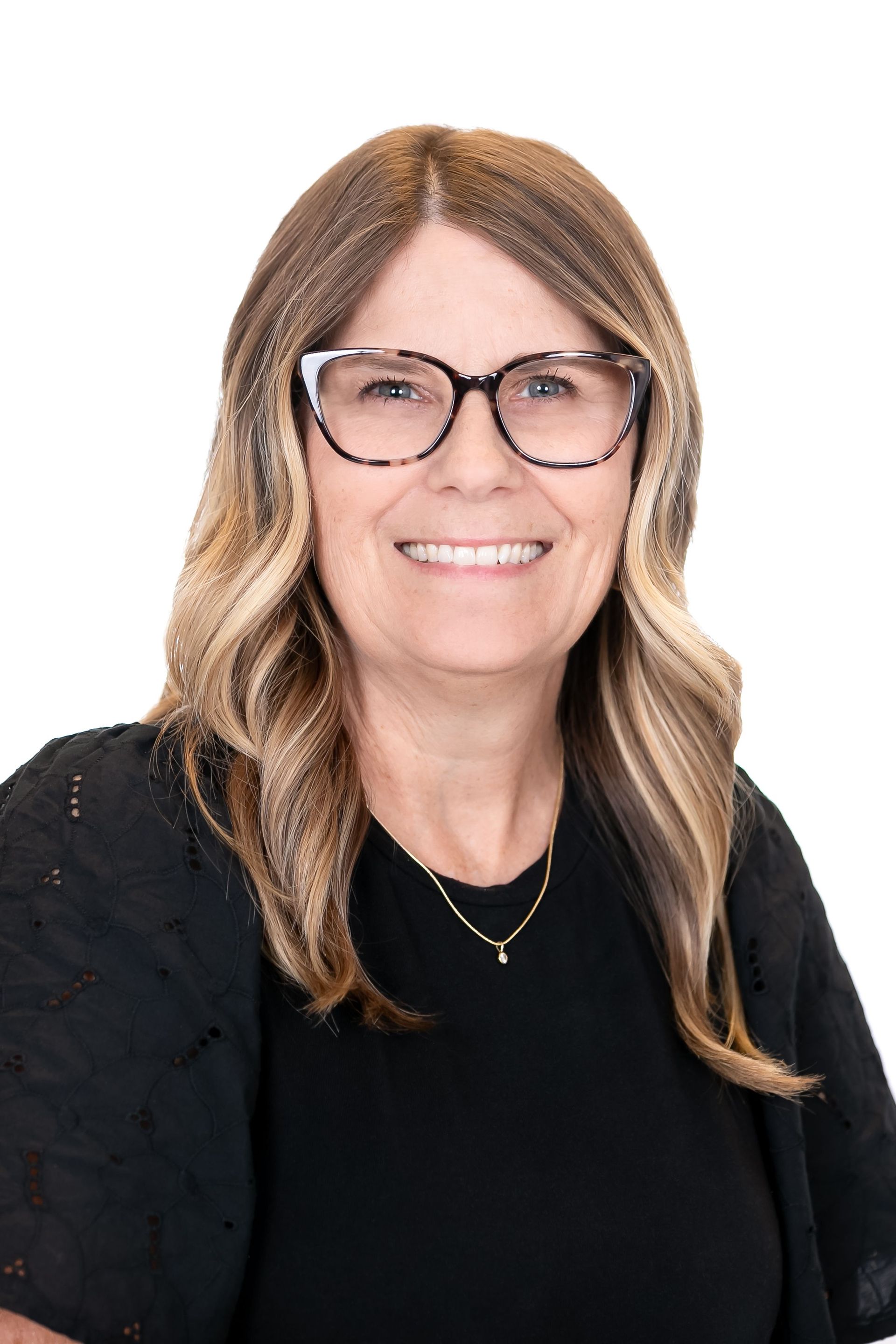 Smiling woman with glasses and wavy hair, wearing a black top against a white background