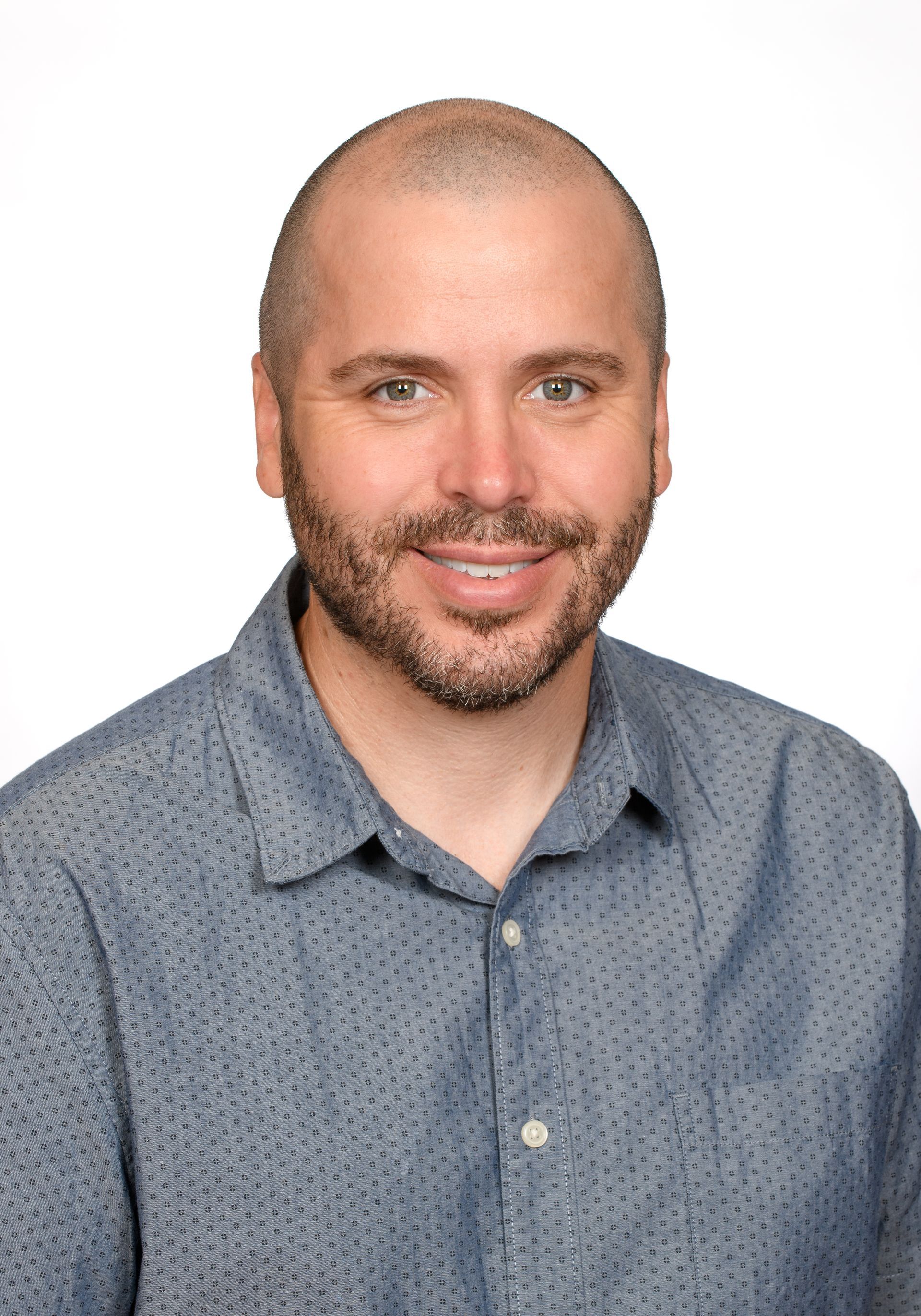 Head-and-shoulders portrait of a smiling man in a blue patterned shirt against a white background
