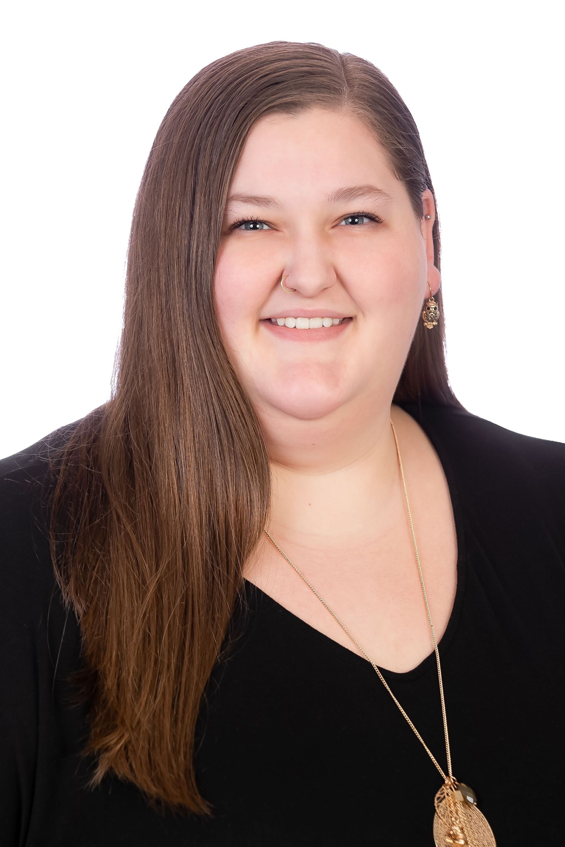 Portrait of a smiling person with long brown hair wearing a black top and gold necklace on a white background