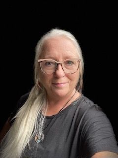 A woman wearing glasses and a necklace is taking a selfie.