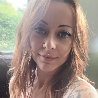 A woman with a nose ring and a tattoo on her arm is smiling for the camera.
