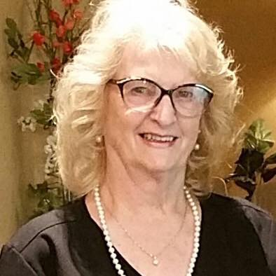A woman wearing glasses and a pearl necklace is smiling for the camera.