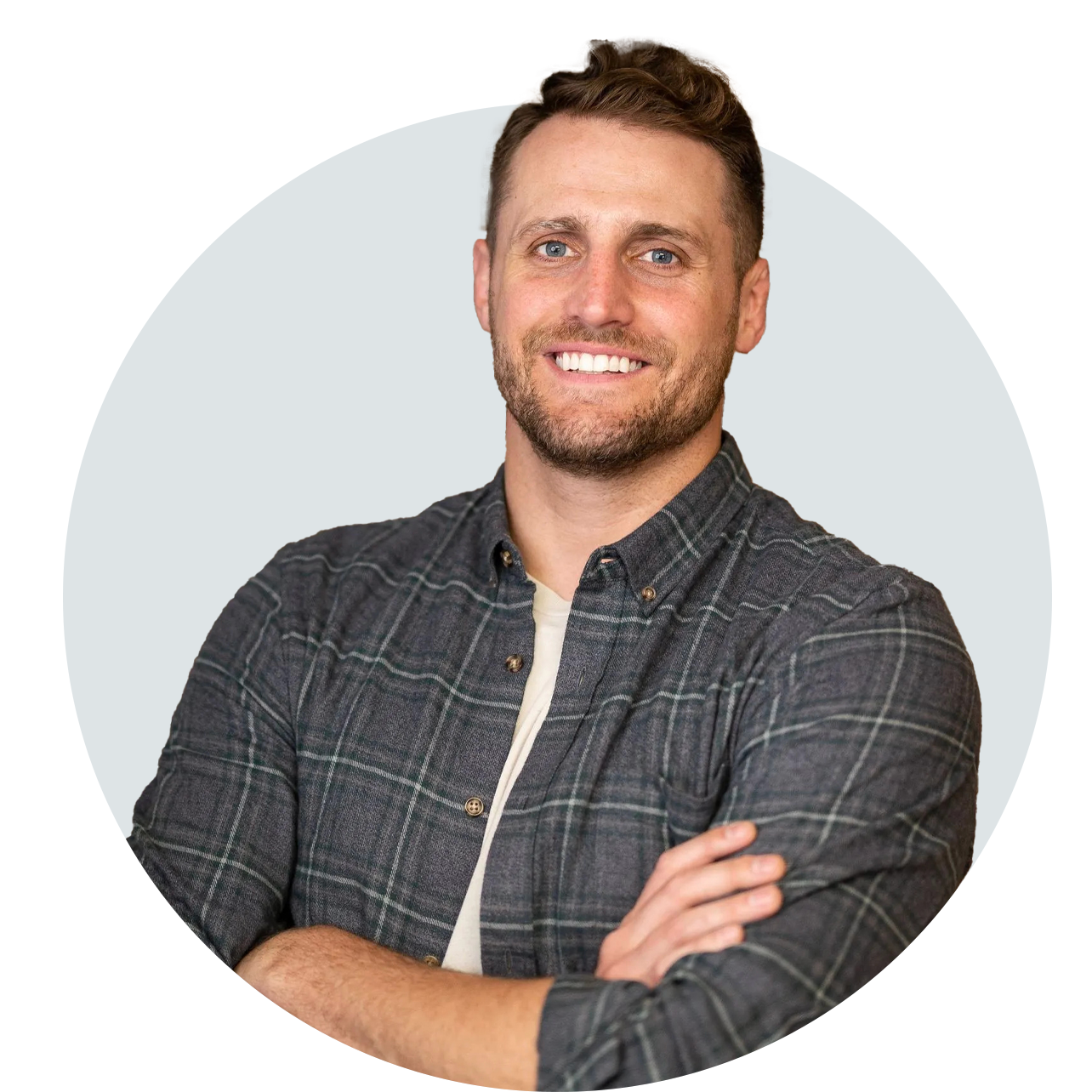 A man in a plaid shirt is smiling with his arms crossed.