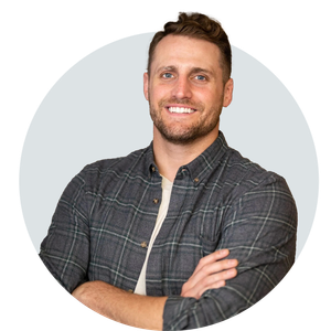 A man in a plaid shirt is smiling with his arms crossed.