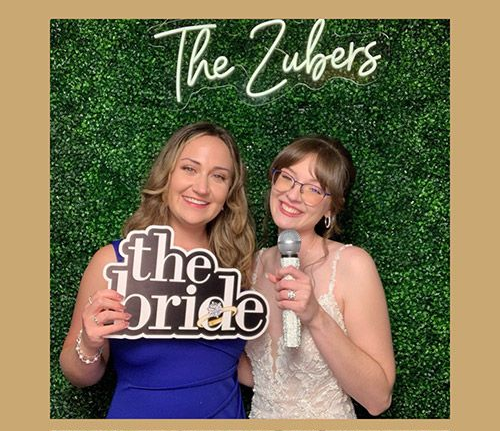 Two smiling women pose at a wedding photo booth.
