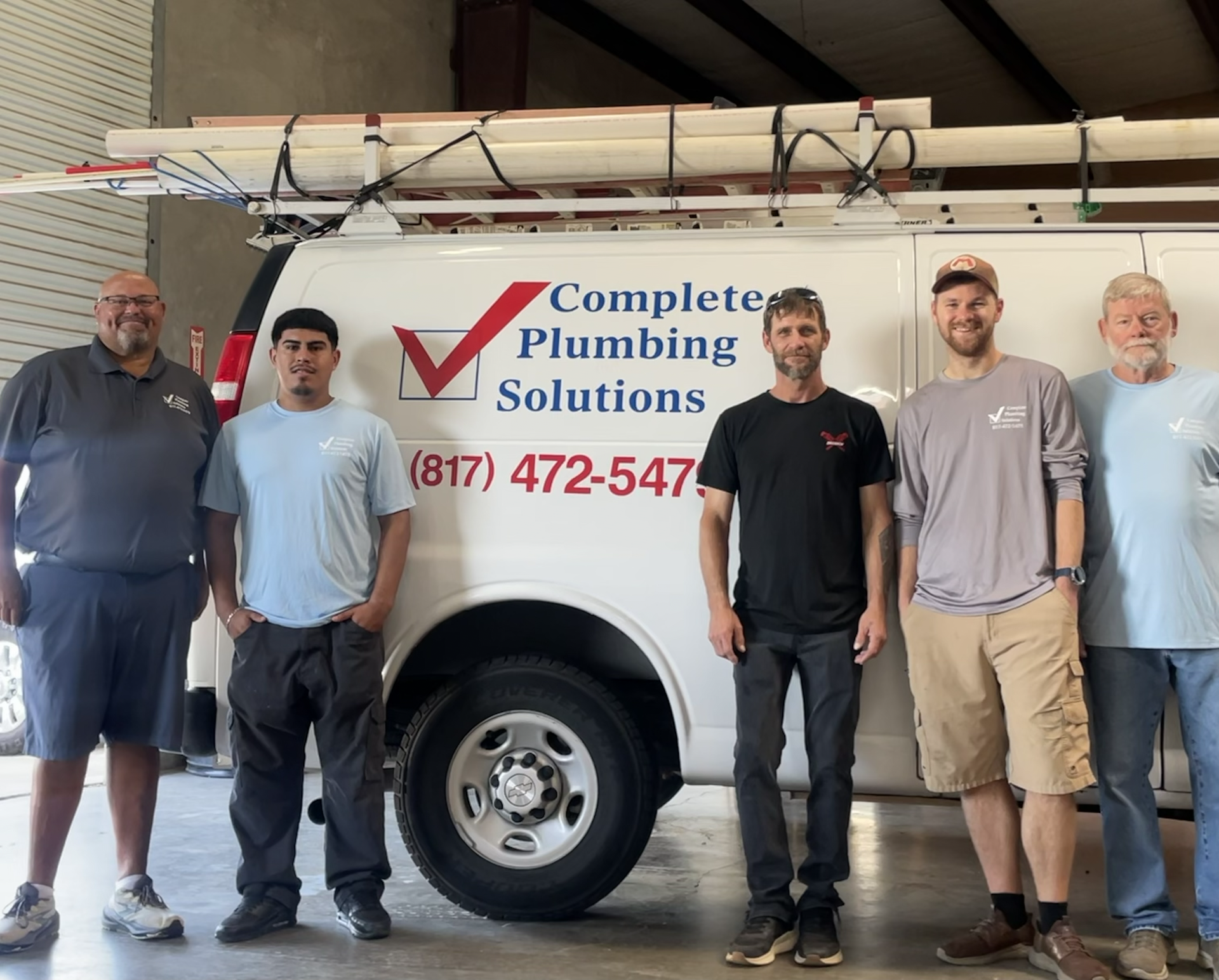 Five men standing in front of a Complete Plumbing Solutions service van in a garage.
