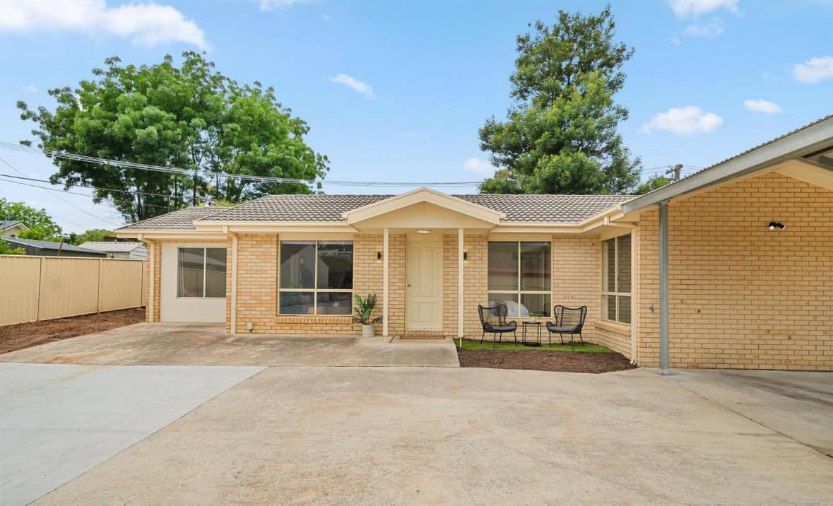 A brick house with a driveway and a table and chairs in front of it.