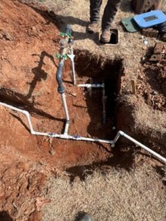 Trenched dirt ground with white PVC pipes and a small blue box beside an excavation hole
