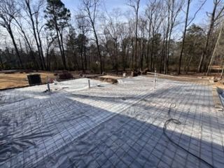 Concrete foundation slab with wire mesh and plumbing stubs at a wooded construction site