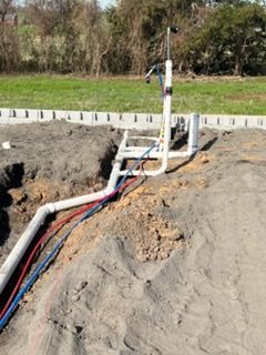 Trenched utility pipes in red, blue, and white at a construction site with grass and trees in the background