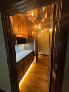 Warm-toned narrow kitchen hallway with dark wood cabinets, marble counter, and hanging pendant lights
