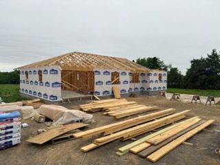 Partially built wooden house frame with roof trusses and lumber stacked on a construction site