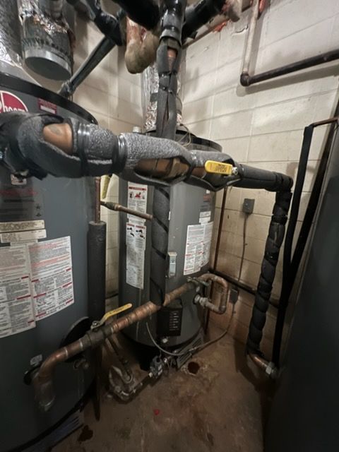 Basement utility room with insulated pipes, water heater, and HVAC equipment against cinder block walls