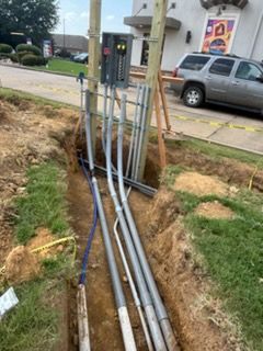 Open trench with exposed utility pipes and conduit beside a street and parked pickup truck.