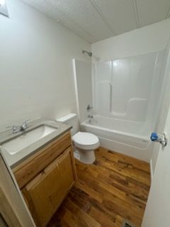 Small bathroom with white tub, toilet, sink vanity, and wood flooring