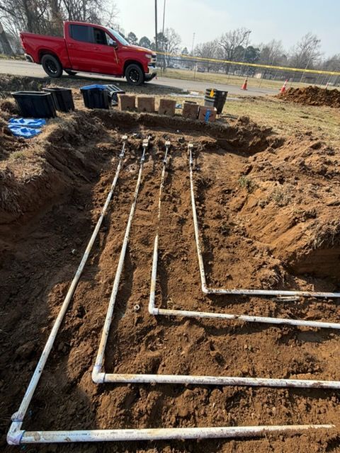 Trenched yard with white PVC pipes laid in parallel, next to a red pickup and stacked blocks.