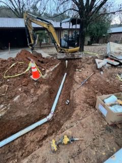 Backyard excavation with mini excavator, open trench, PVC pipe, and orange traffic cone near a house