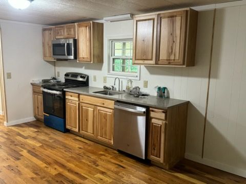 Compact kitchen with wood cabinets, stainless steel appliances, and hardwood floors.