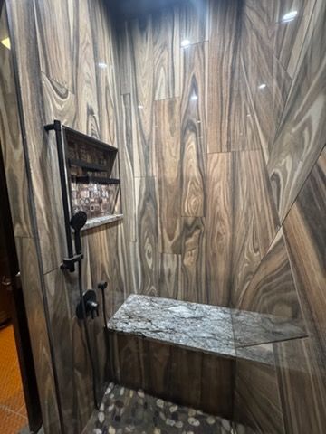 Compact wood-paneled shower with a granite bench, shelf, and handheld showerhead.