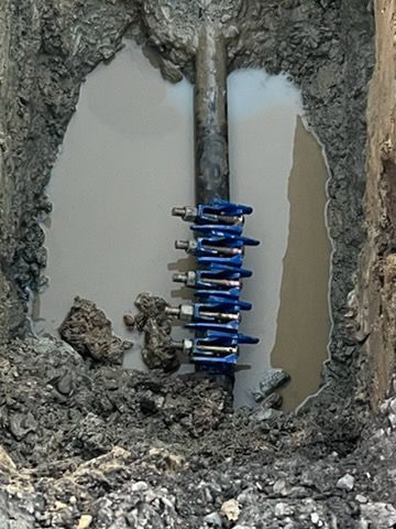 Blue spring coil attached to a pipe inside a muddy excavated trench