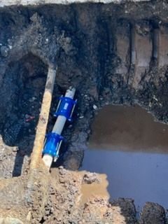 Excavation trench with a blue pipe section and muddy water beside exposed soil and rock formations
