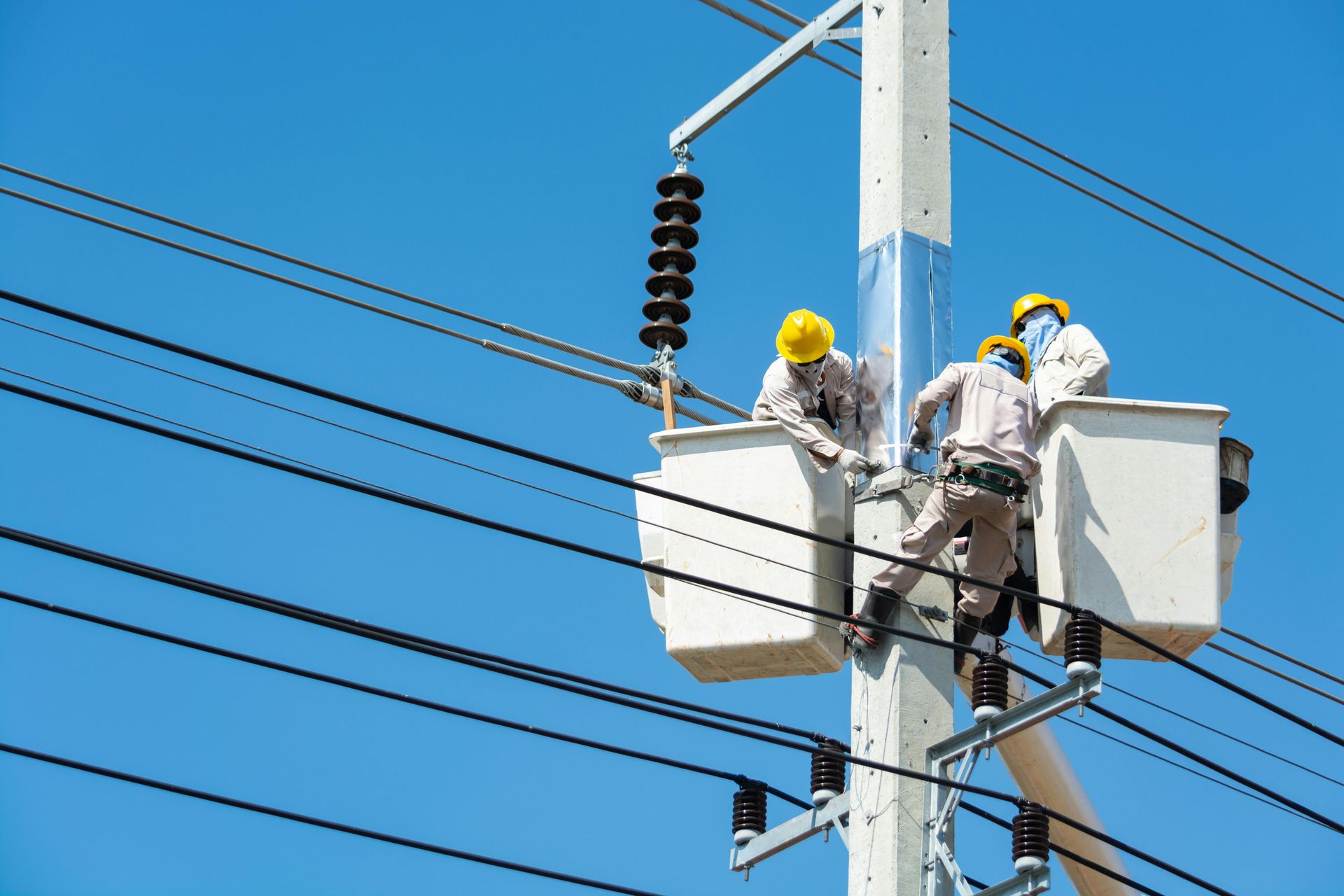 Utility workers in bucket trucks repairing power lines on a pole against a blue sky