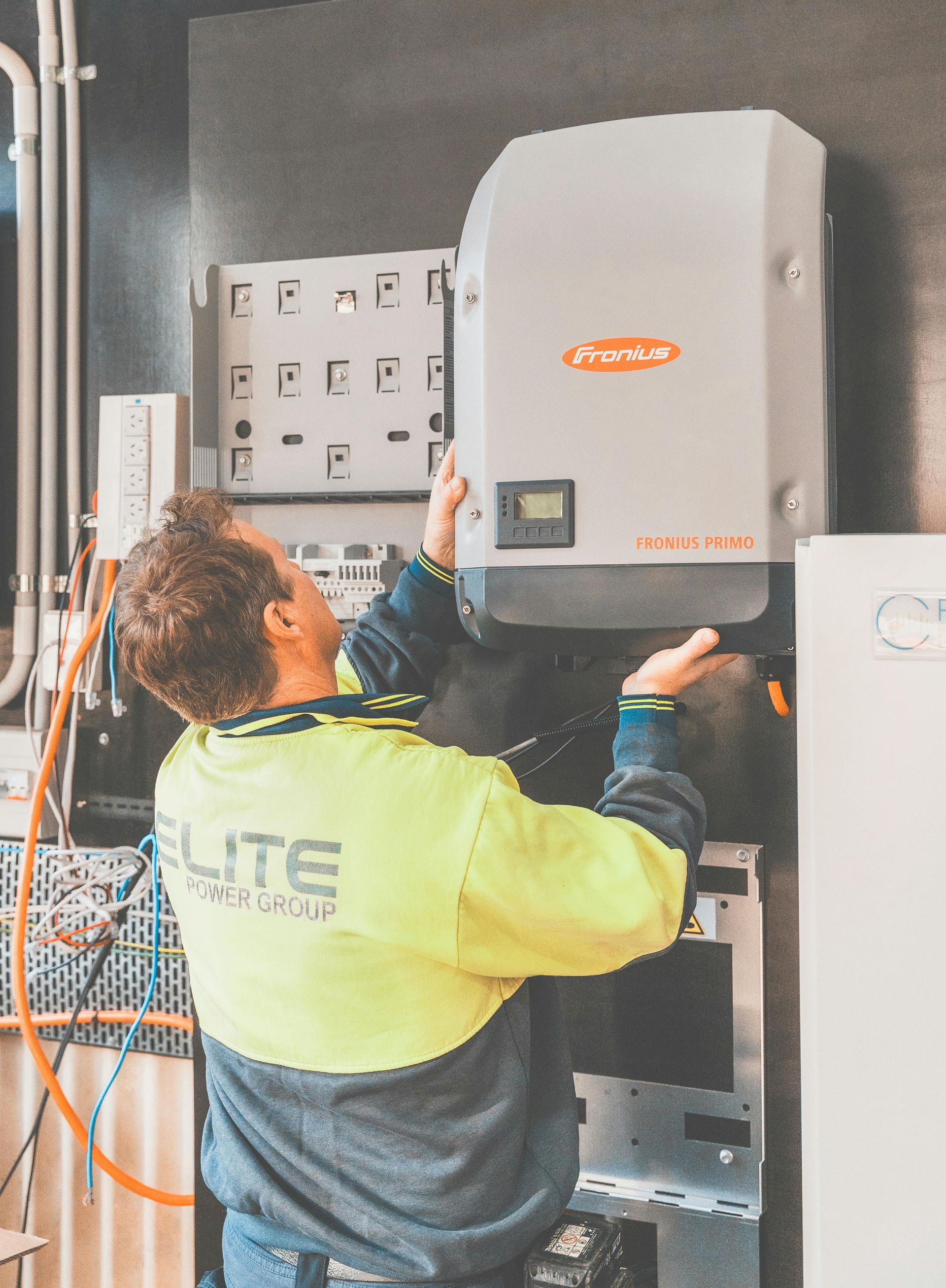 Technician in a yellow jacket inspecting a wall-mounted electrical cabinet in an industrial room