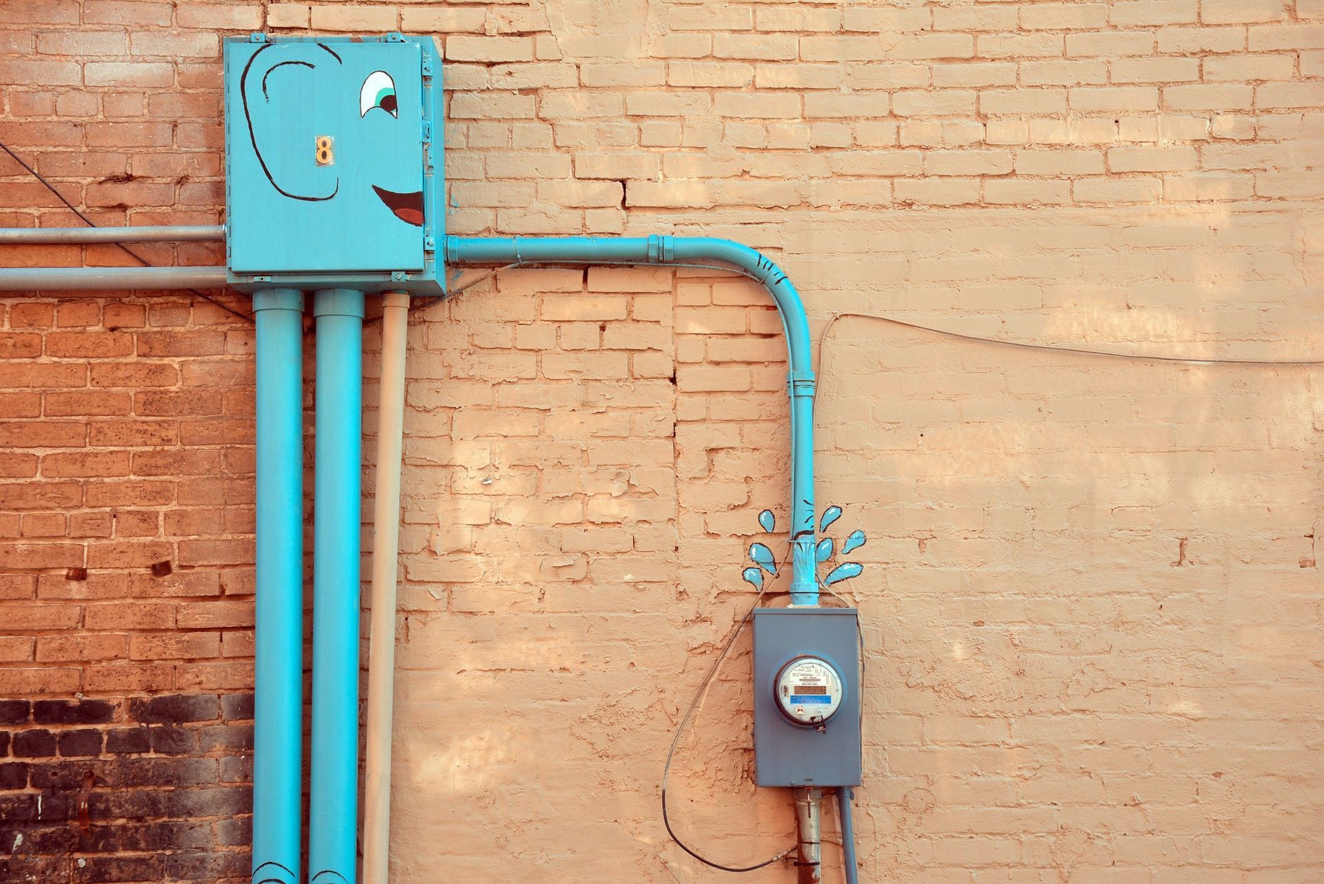 Turquoise electrical conduit and meter boxes on a tan brick wall