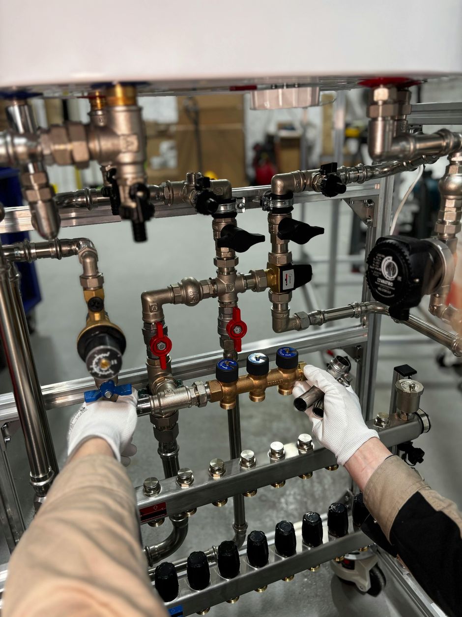 Gloved hands adjusting valves and pipes on an industrial plumbing manifold in a mechanical room