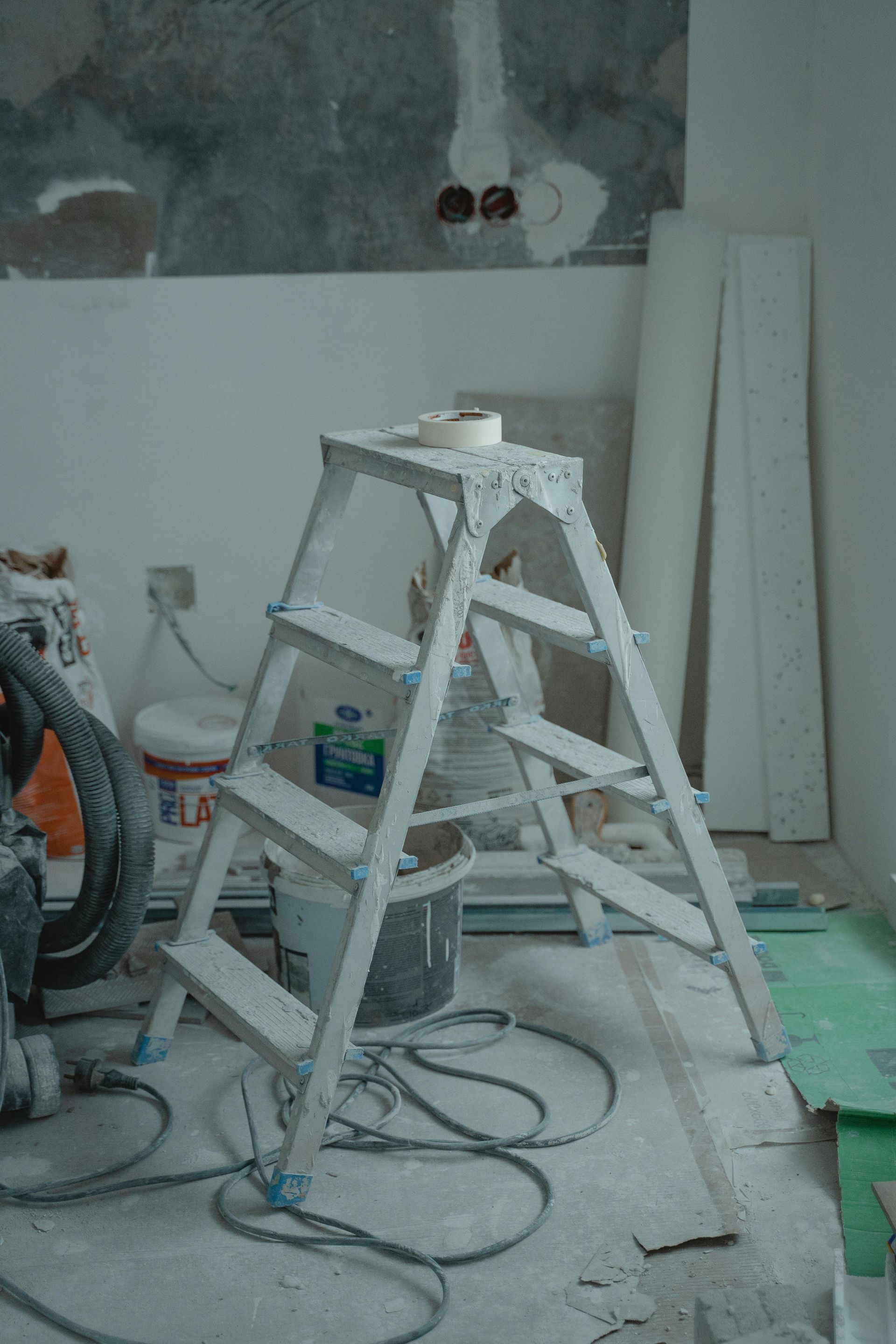 Painting/worksite with a white step ladder, tools, cables, and unfinished walls and floor