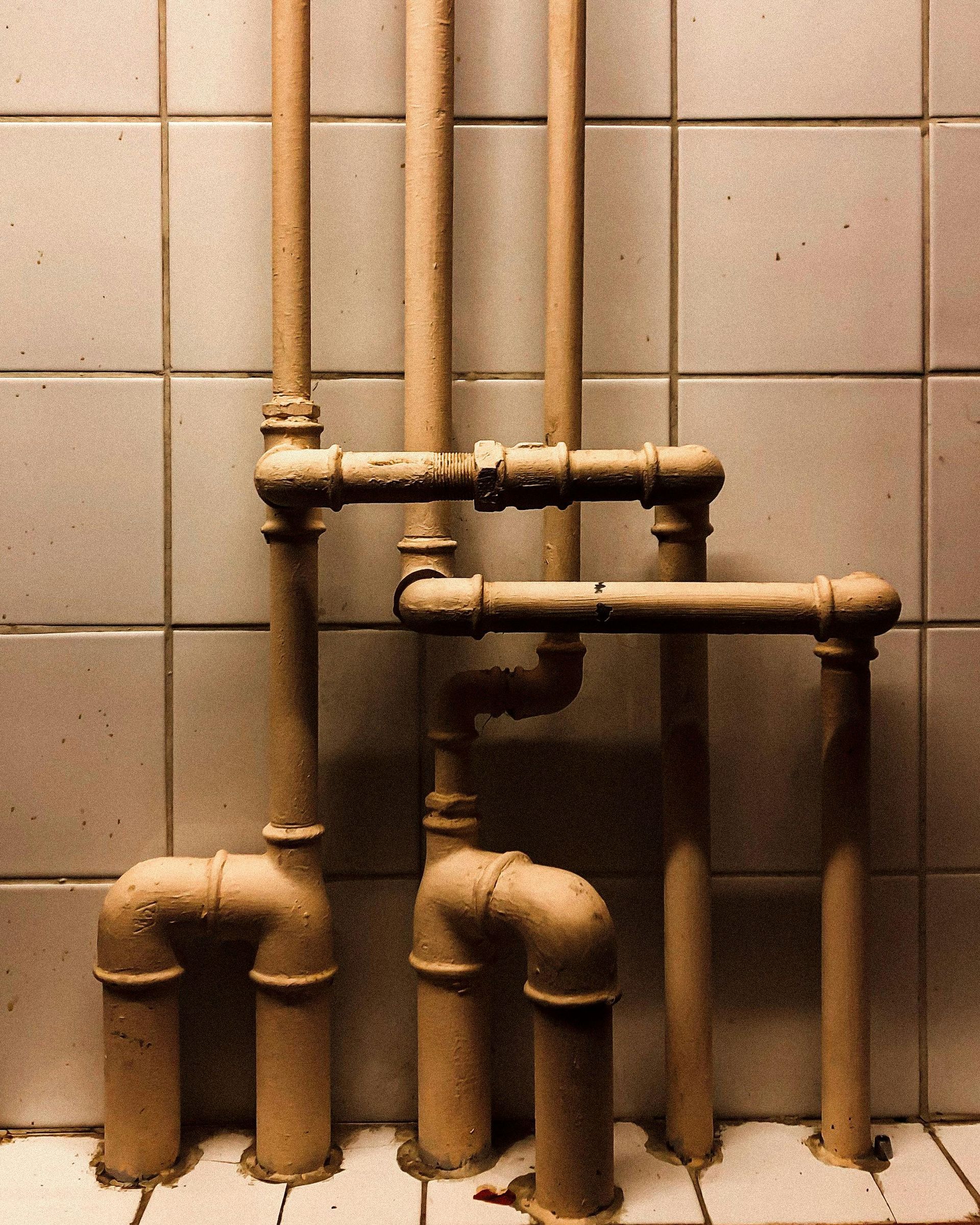 Old beige wall tiles with exposed copper pipes and fittings in a bathroom or utility room.