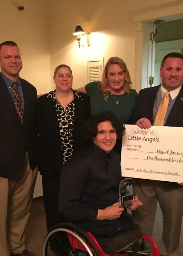 Group with check and award. Man in wheelchair holds award. Others smile, pose with check for 