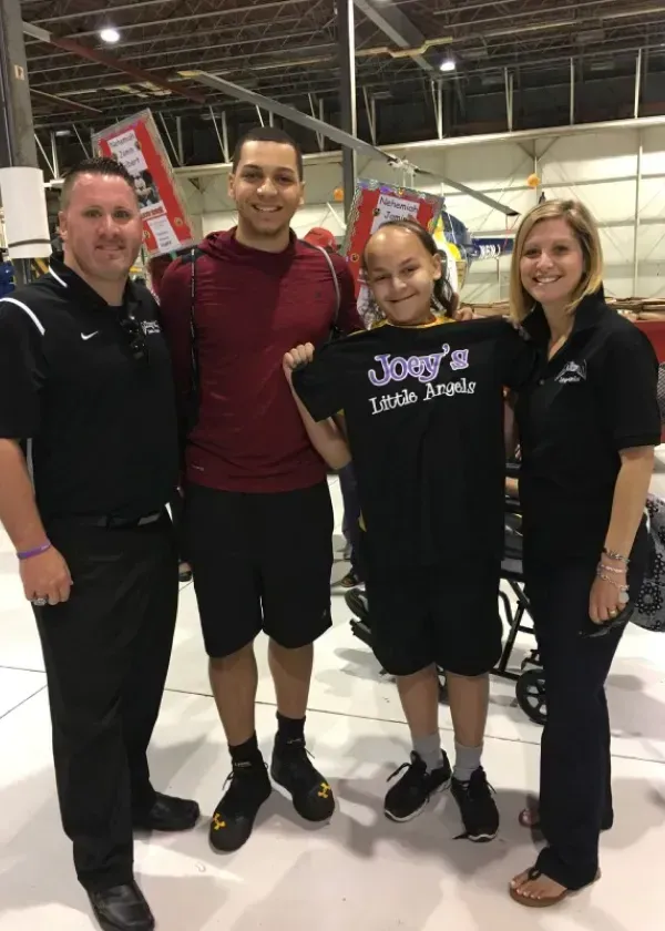 Four people pose for a photo in front of a helicopter. One holds a 