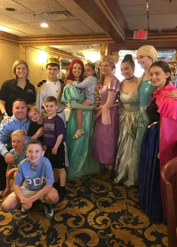 Group posing with princess characters in a restaurant, including Ariel and Elsa.