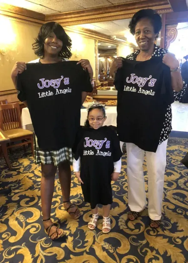 Three people, including a child, hold up matching black shirts with 