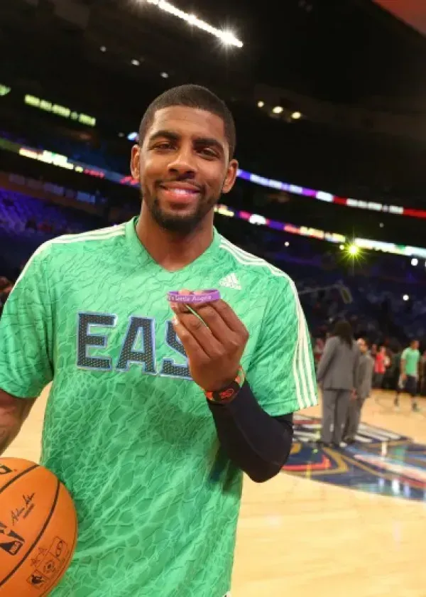 Kyrie Irving holding a purple candy, smiling, in an arena wearing a green 