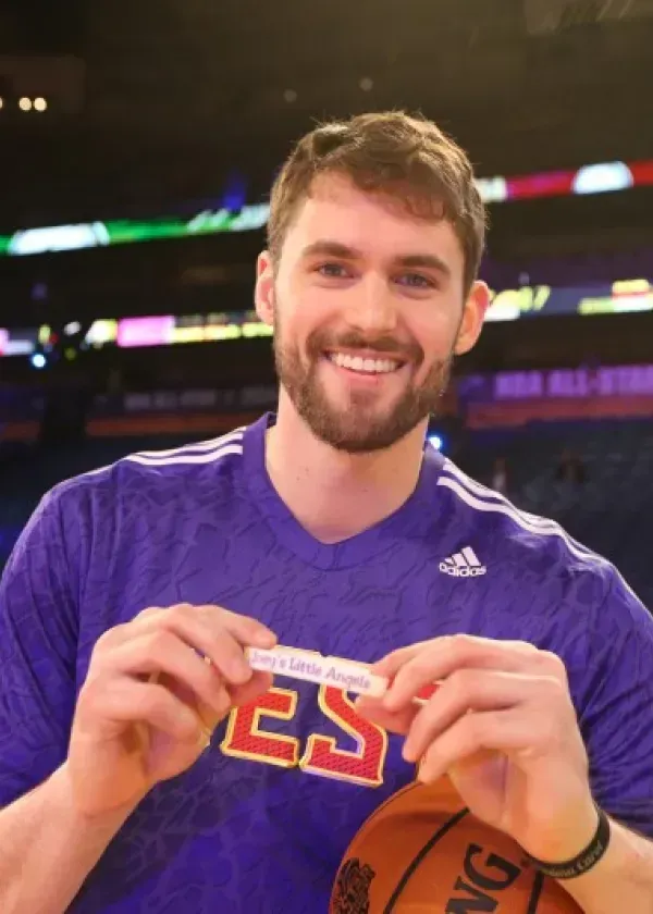 Basketball player Kevin Love holding a sign, smiling at a court.