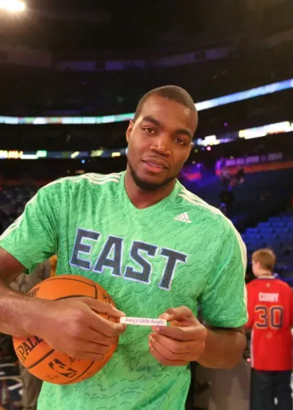 Basketball player holding a basketball and a small paper, wearing a green 