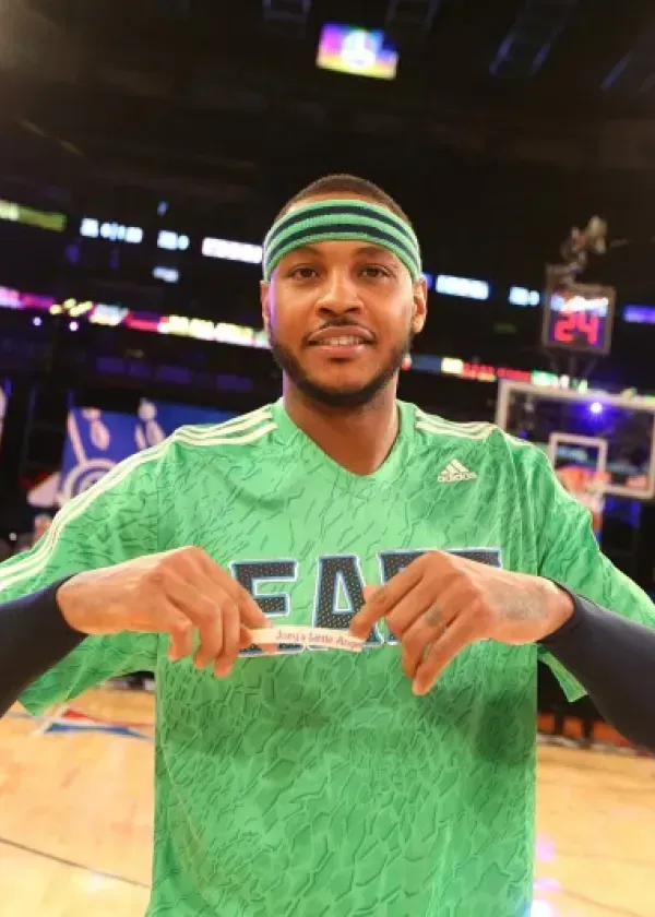 Basketball player holding a promotional item, wearing a green headband and shirt, smiling.